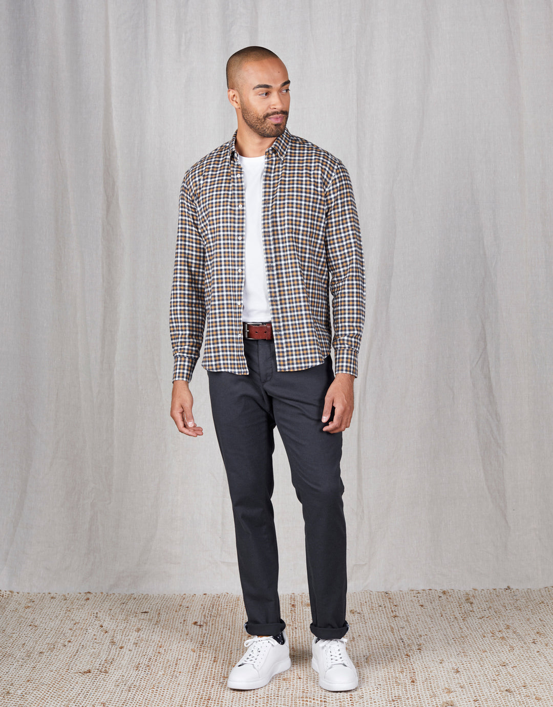 Men's plaid button-up shirt with white tee, dark chinos, brown belt, white sneakers — casual fashion outfit