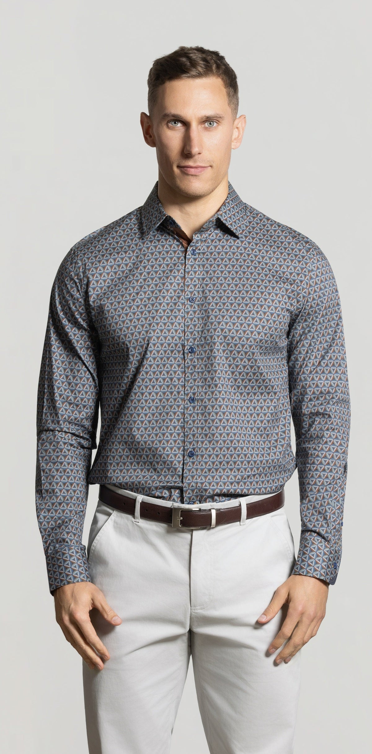 Man wearing a patterned shirt and light pants against a plain background