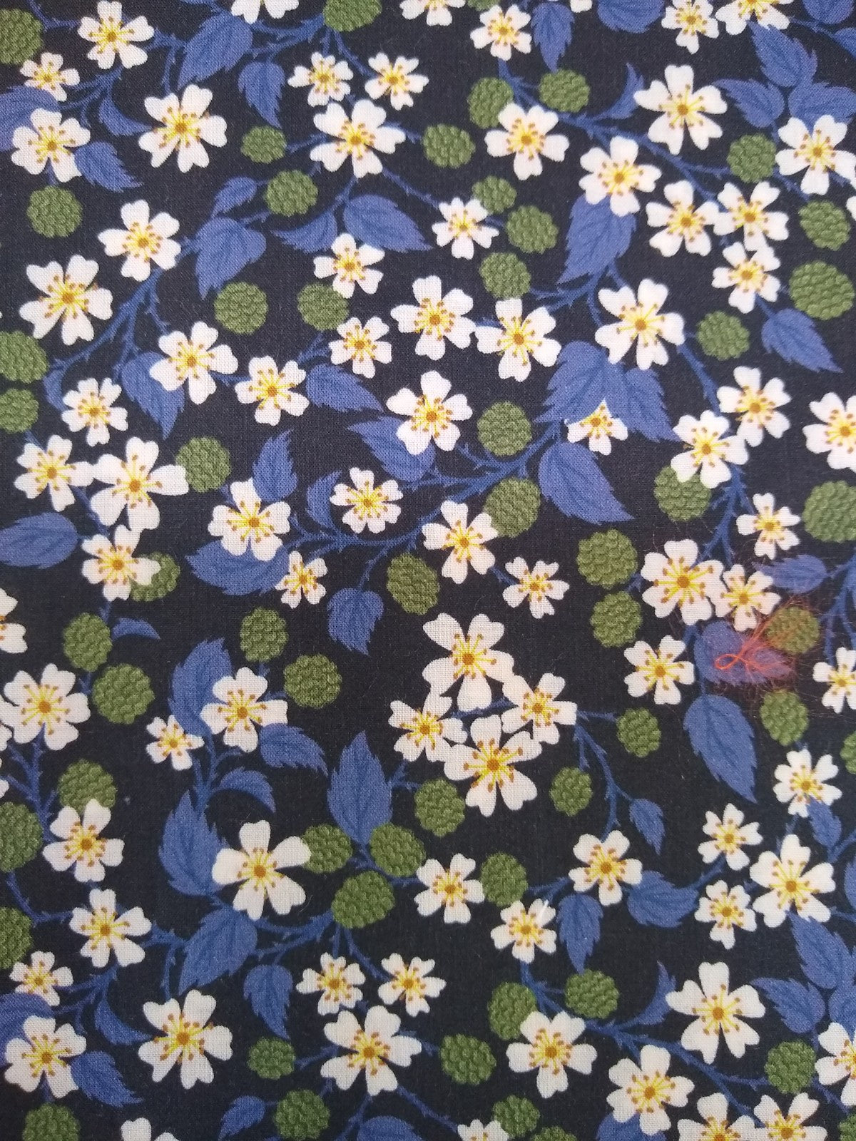 Floral fabric with white flowers, blue leaves, and green berries on dark background for women's fashion clothing
