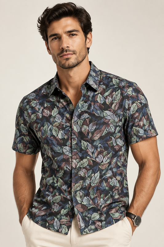 A folded long-sleeve button-up shirt by Cambridge (UK) featuring an all-over abstract leaf pattern in muted shades of blue, green, brown, and beige on a dark background, displayed on a wooden surface.
