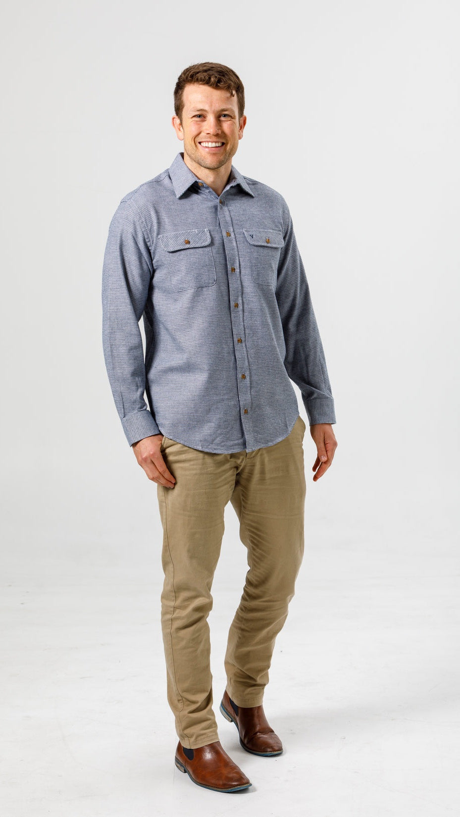 Man wearing a blue flannel shirt and beige pants on a white background