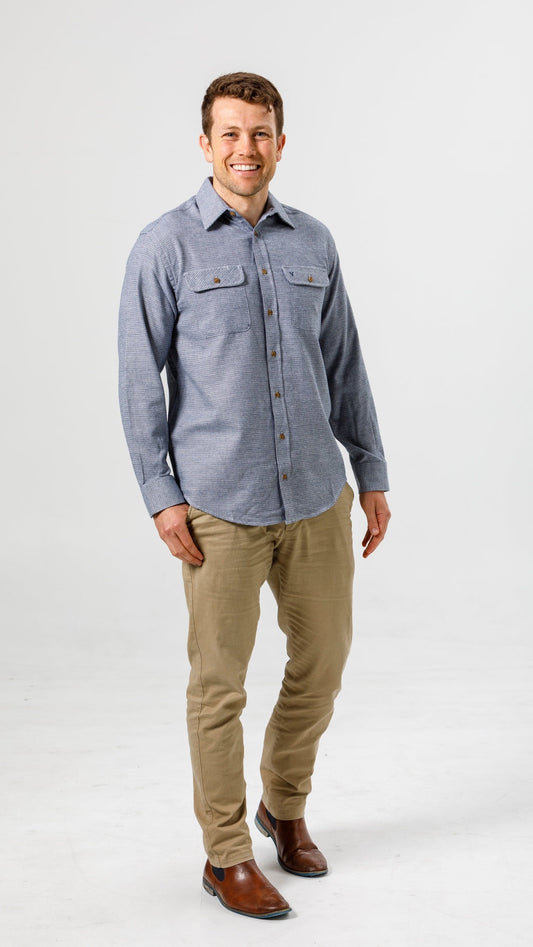 Man wearing a blue flannel shirt and beige pants on a white background