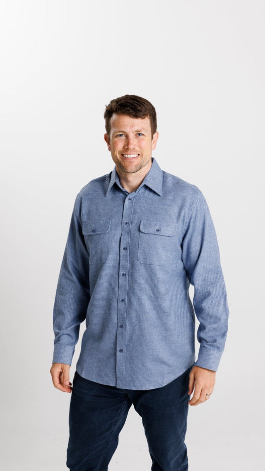 Man wearing a blue button-up shirt and dark pants on a white background