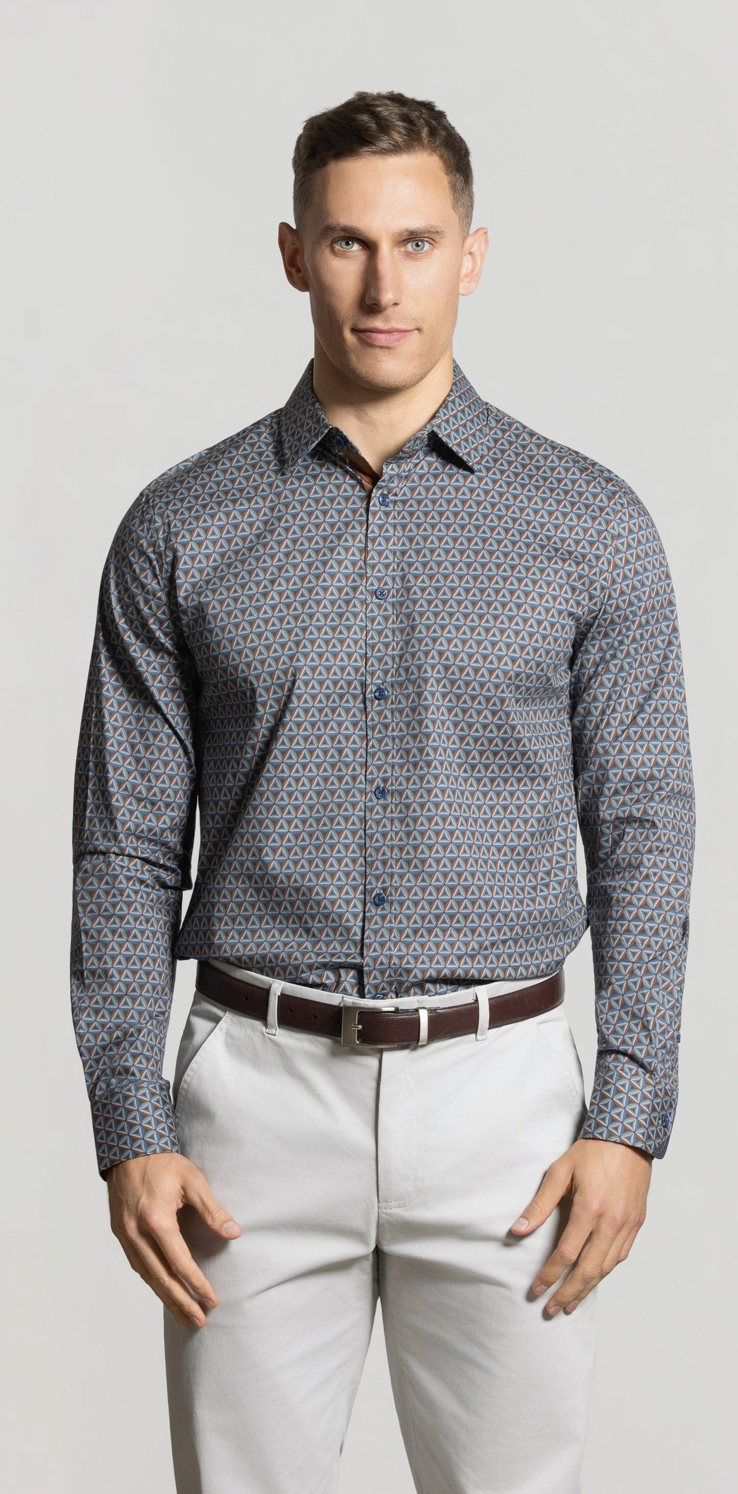 Man wearing a patterned shirt and light pants against a plain background