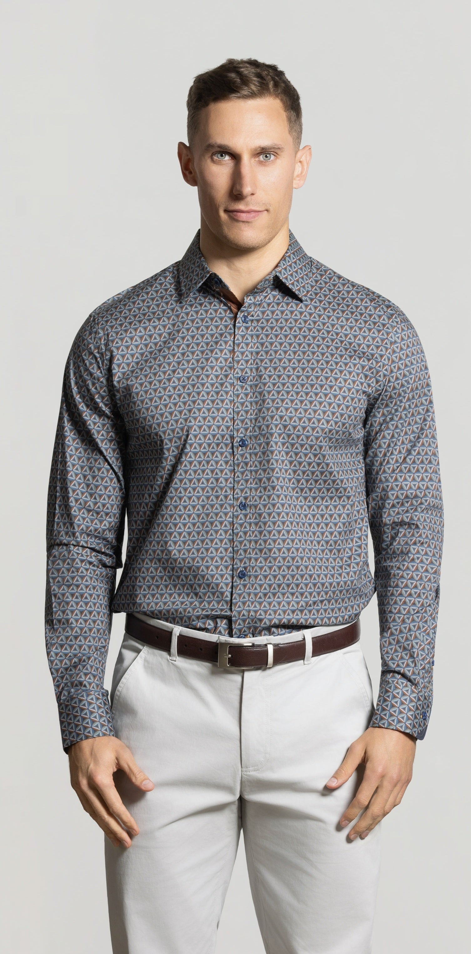 Man wearing a patterned shirt and light pants against a plain background