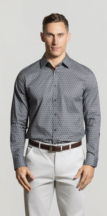 Man wearing a patterned shirt and light pants against a plain background